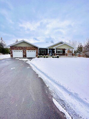 A two-story house with a garage, a covered porch, and a snow-covered driveway. - Cozy Retreat On The Eastside Estate (sleeps 4) (Greater Napanee)