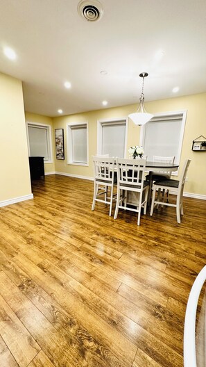 A dining area with a wooden floor, white chairs, a table, and a hanging light fixture. - Cozy Retreat On The Eastside Estate (sleeps 4) (Greater Napanee)
