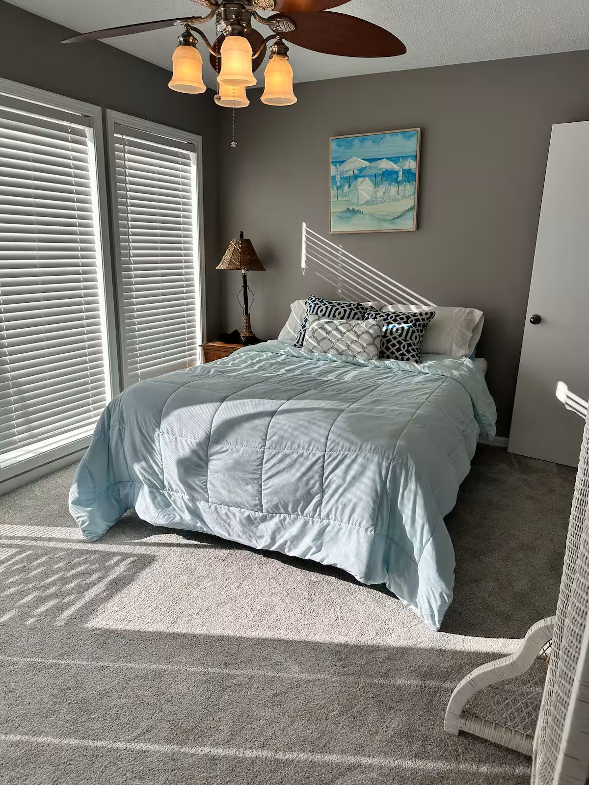 A bedroom with a bed, a ceiling fan, a nightstand, a lamp, and a painting on the wall.