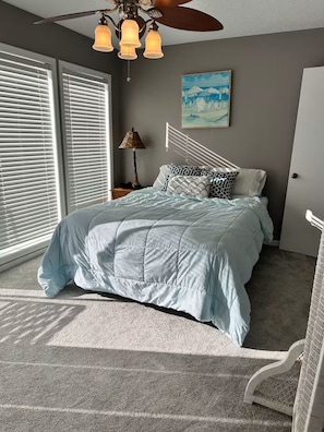 Ein Schlafzimmer mit Bett, Deckenventilator, Nachttisch, Lampe und einem Bild an der Wand.