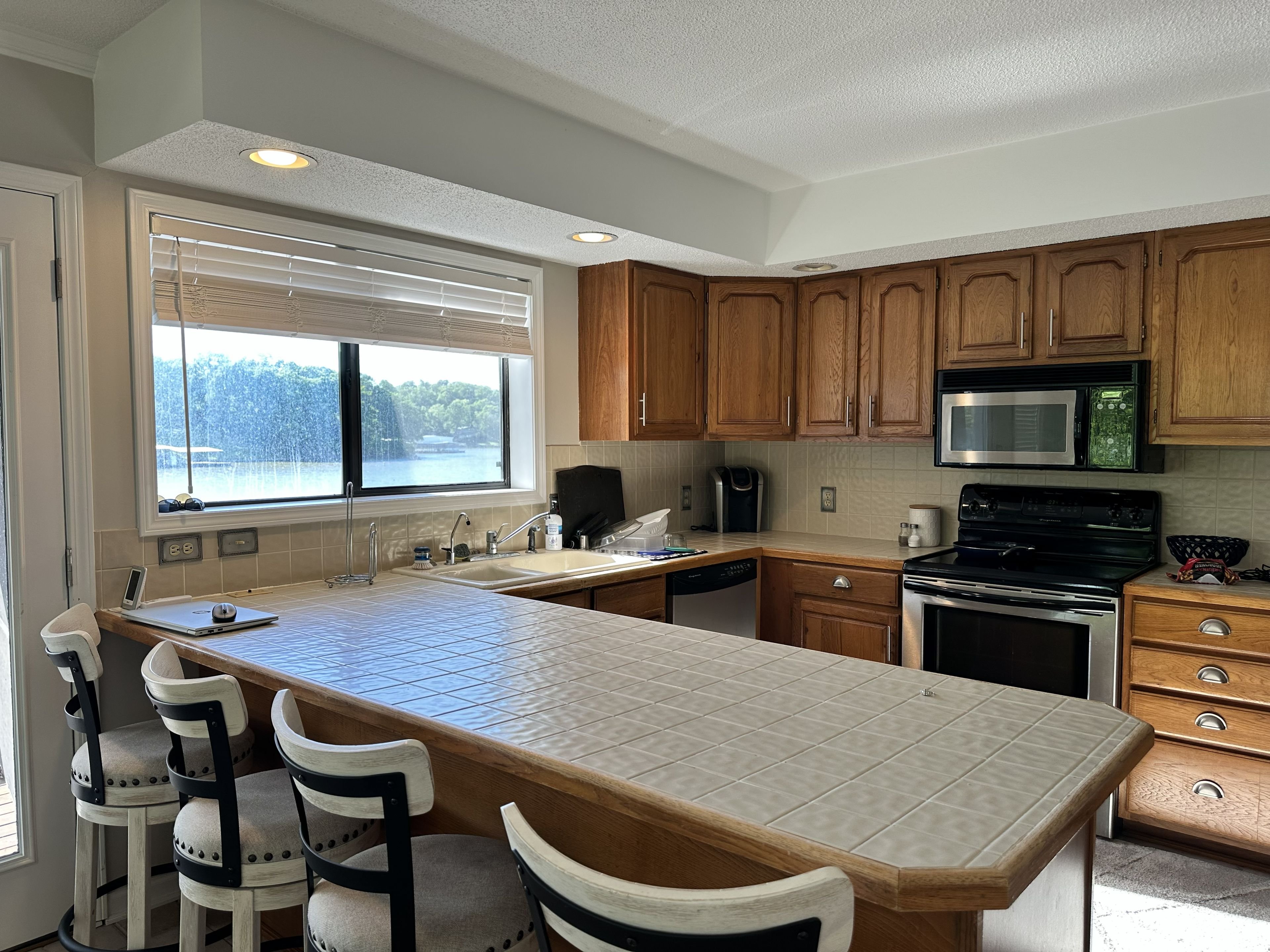 Una cocina con armarios de madera, una isla grande con taburetes de bar, un microondas y vistas a un lago a través de la ventana.