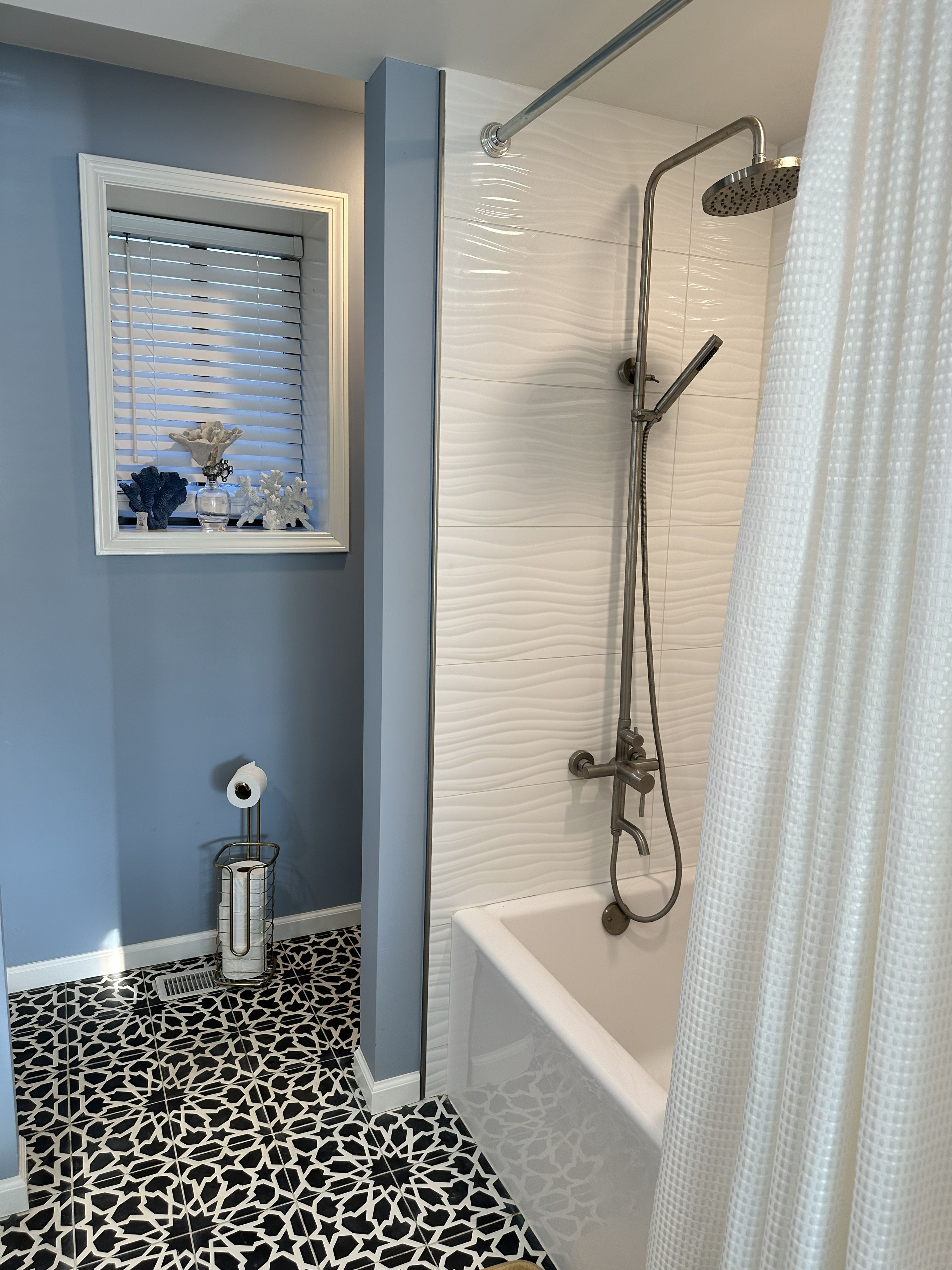Un baño con ducha, inodoro, lavamanos y una ventana con adornos.