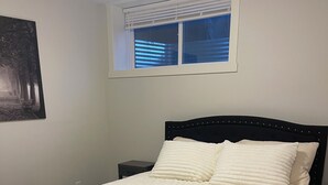 A bedroom with a bed, a nightstand, a window with blinds, and a wall-mounted picture. - Adorable 1-bedroom condo in beautiful Calgary perfect for your stay (Calgary)