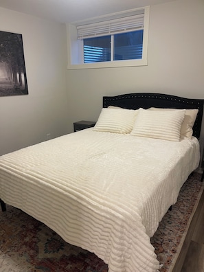 A bedroom with a bed, a nightstand, a window with blinds, and a wall-mounted picture. - Adorable 1-bedroom condo in beautiful Calgary perfect for your stay (Calgary)