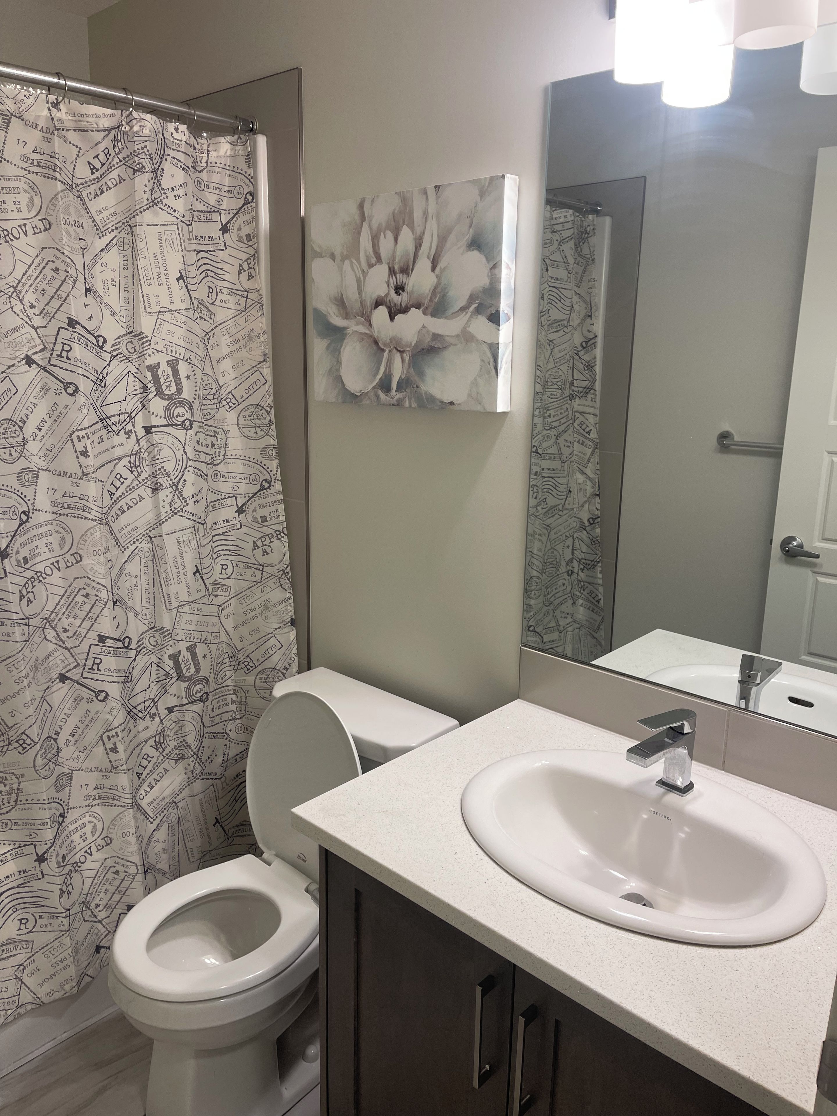Une salle de bain avec des toilettes, un lavabo et un rideau de douche orné de motifs représentant des tampons de voyage.