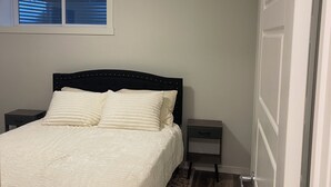 A bedroom with a bed, bedside tables, a window with blinds, and a door. - Adorable 1-bedroom condo in beautiful Calgary perfect for your stay (Calgary)