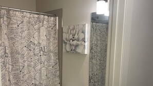 A bathroom with a shower curtain featuring travel stamps, a toilet, a sink with a mirror, and wooden cabinets. - Adorable 1-bedroom condo in beautiful Calgary perfect for your stay (Calgary)