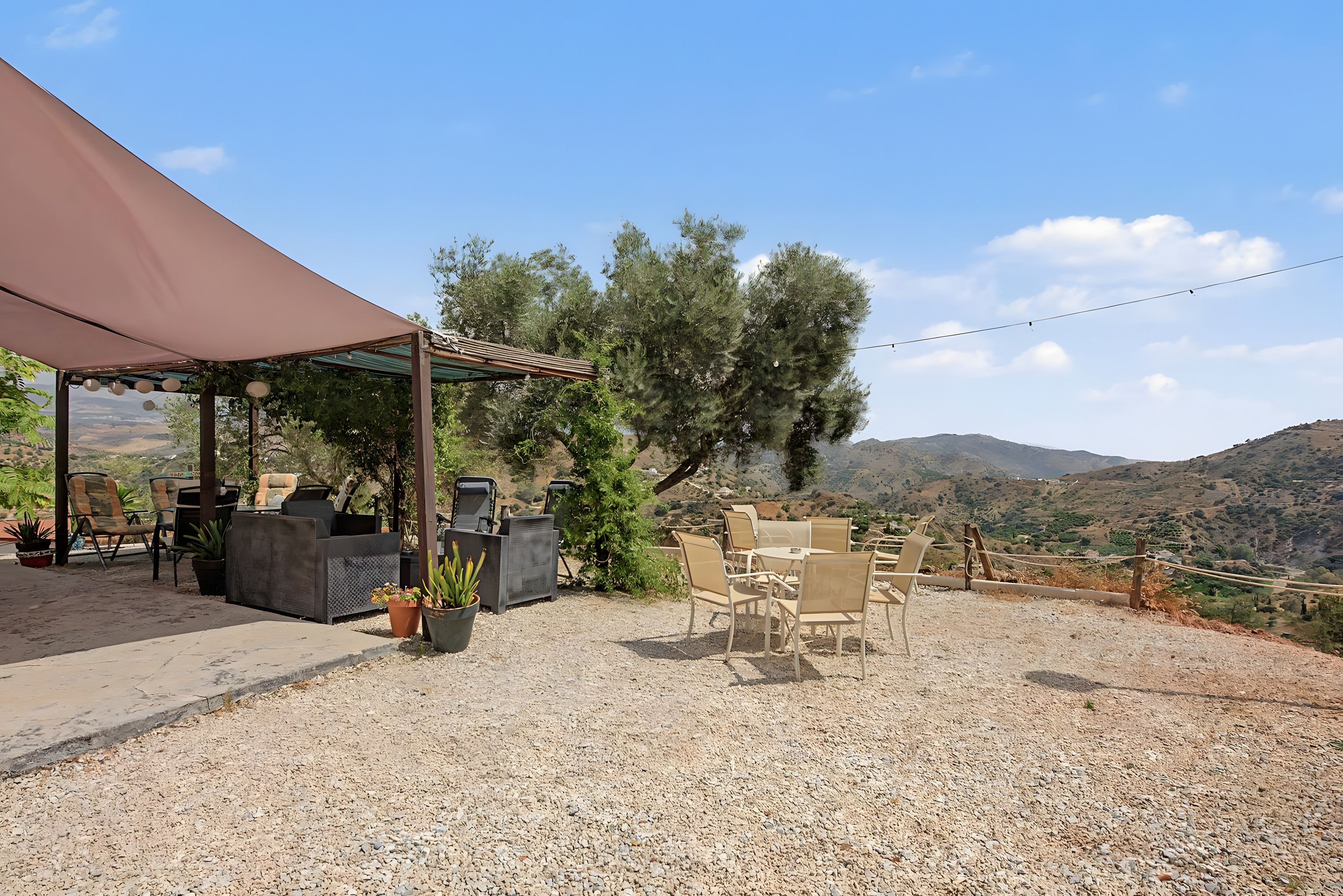 Un espace extérieur aménagé avec des tables et des chaises, une partie abritée et une vue sur le paysage environnant.