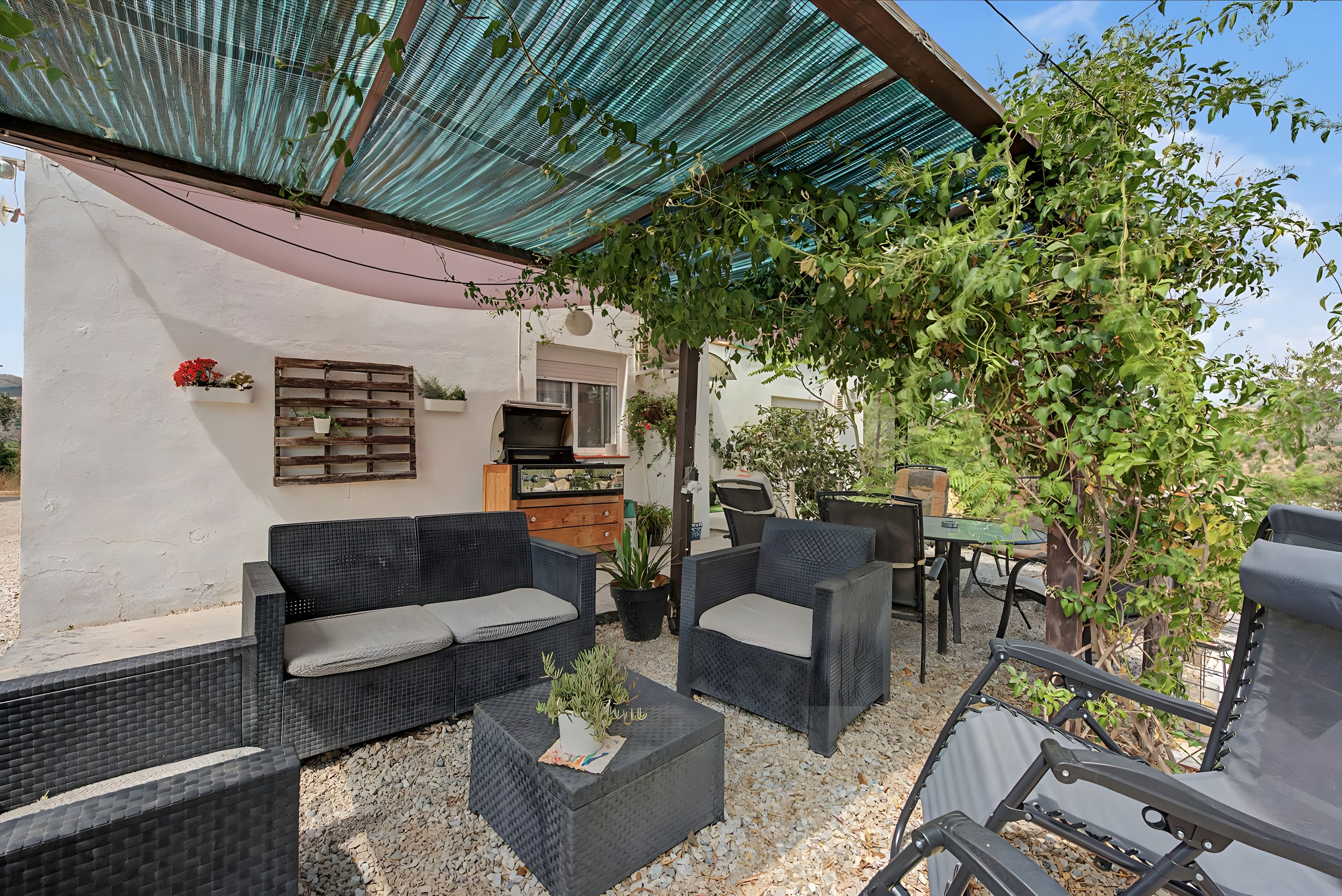 Een terras met rieten meubels, een houten tafel en potplanten.