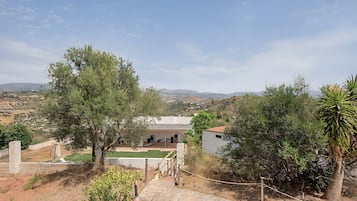 Una propiedad residencial con un camino pavimentado que lleva a una casa con paneles solares en el techo, rodeada de árboles y un paisaje montañoso.