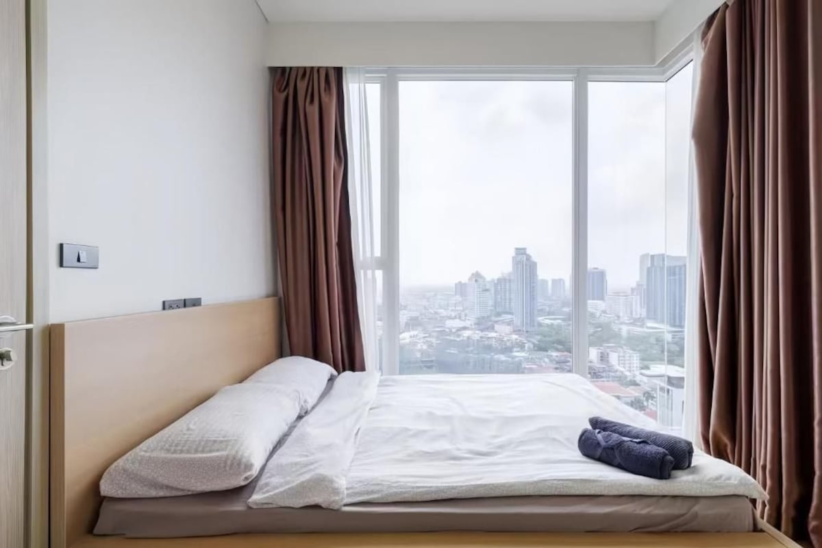 A hotel room with a bed, a window with curtains, and a city view.