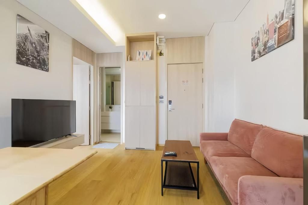 A modern living room with a flat-screen TV, a sofa, a coffee table, and a door leading to a kitchen.