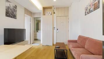 A modern living room with a flat-screen TV, a sofa, a coffee table, and a door leading to a kitchen.