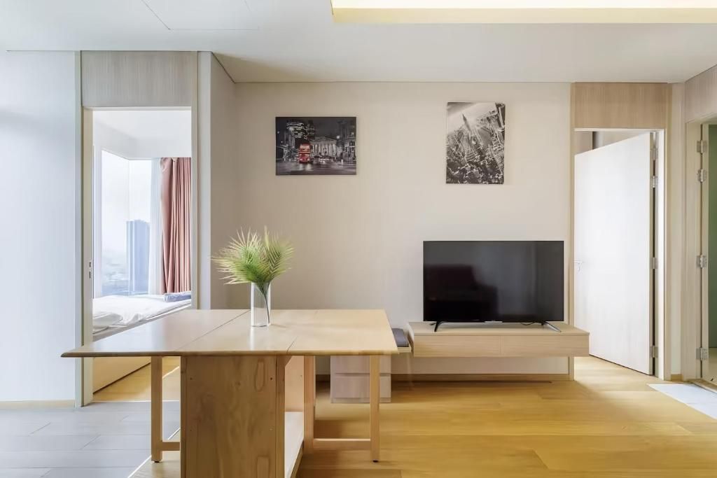 A modern living room with a wooden floor, a flat-screen TV, a small table with a vase, and two wall-mounted pictures.