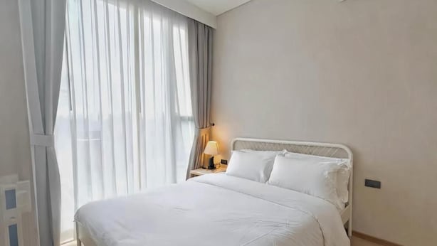 Et hotelværelse med en seng, et natbord, en lampe og et vindue med gardiner.