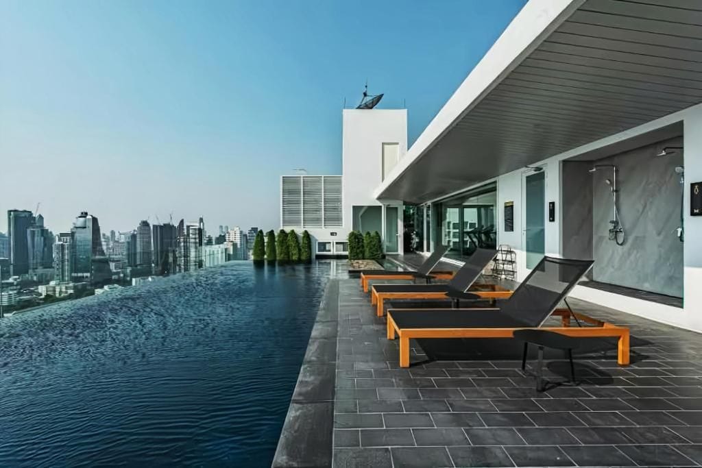 A rooftop infinity pool with lounge chairs, a city skyline view, and modern architecture.