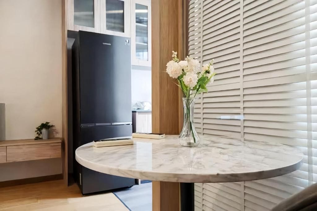 A kitchen with a marble countertop, a black refrigerator, and a vase with flowers on the counter.