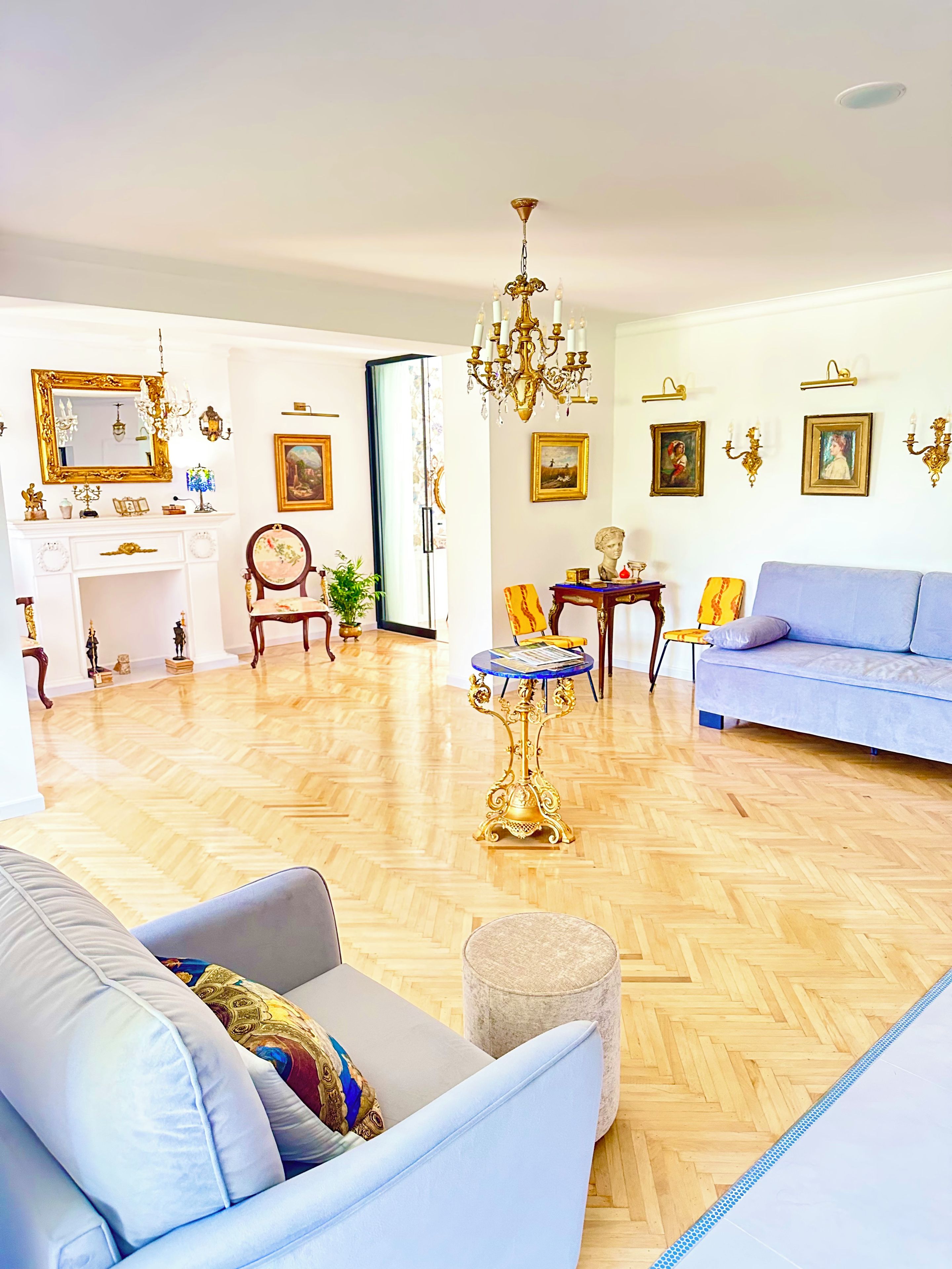A spacious living room with a blue sofa, a chandelier, and a fireplace.