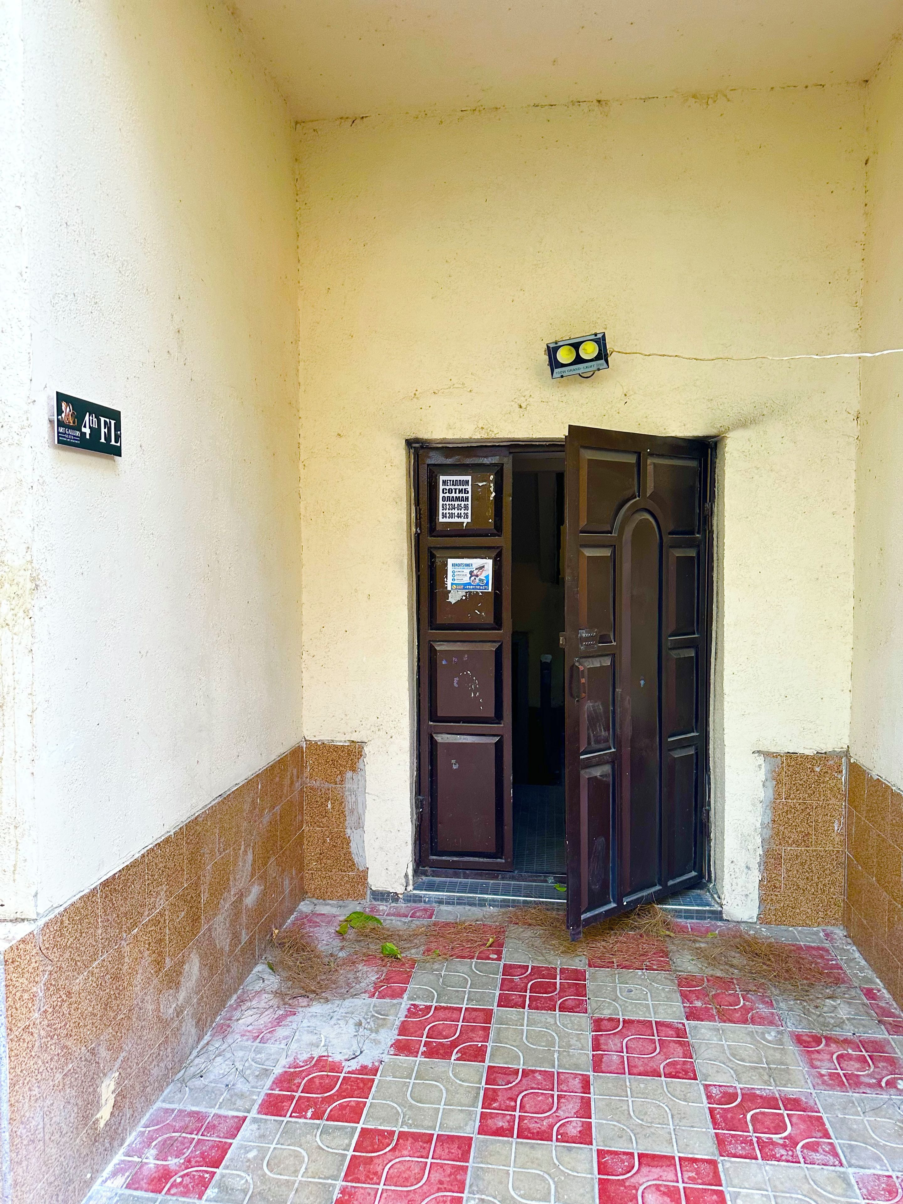 Entrada d'un edifici amb un paviment de rajoles, una porta i un rètol a la paret.
