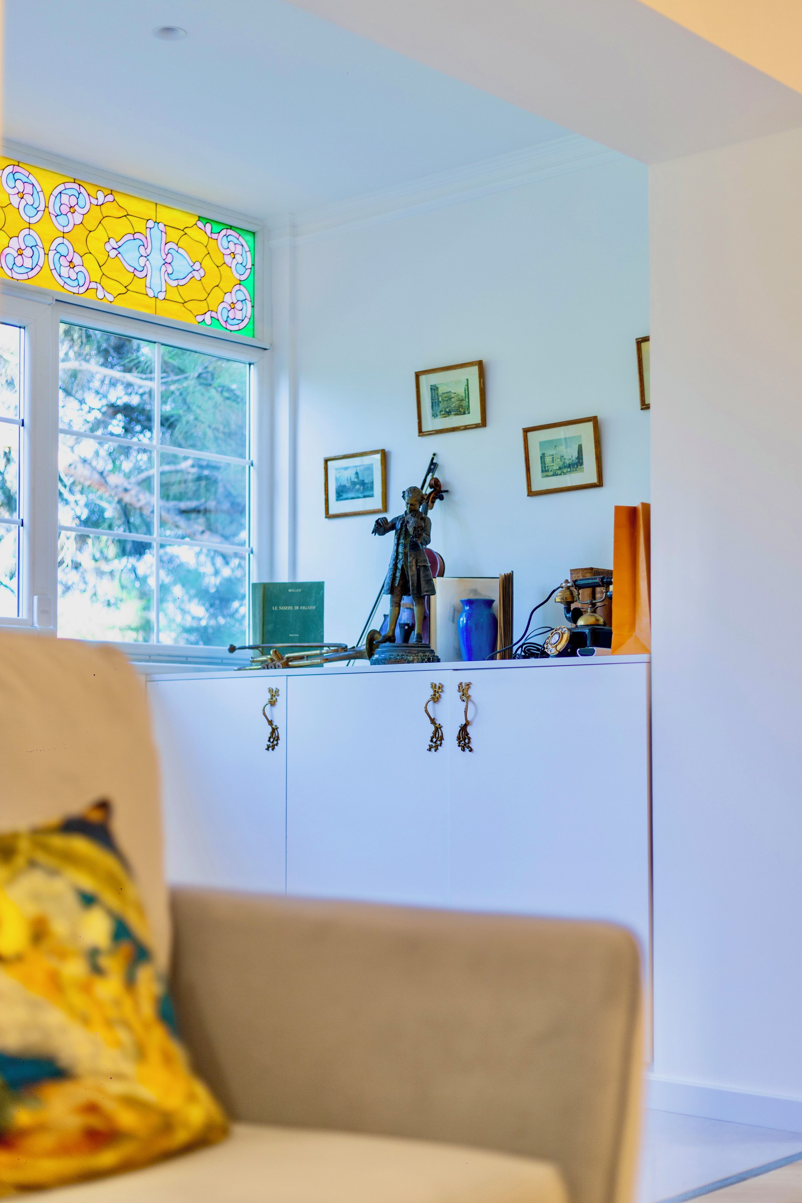 Une pièce avec une fenêtre, une statue, des tableaux encadrés et un vase décoratif.