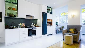 A modern kitchen with white cabinetry, a herringbone wood floor, and a dining area with a grey armchair and ottoman.