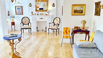 A room with a herringbone wooden floor, a blue sofa, a gold ornate table, and a chandelier.