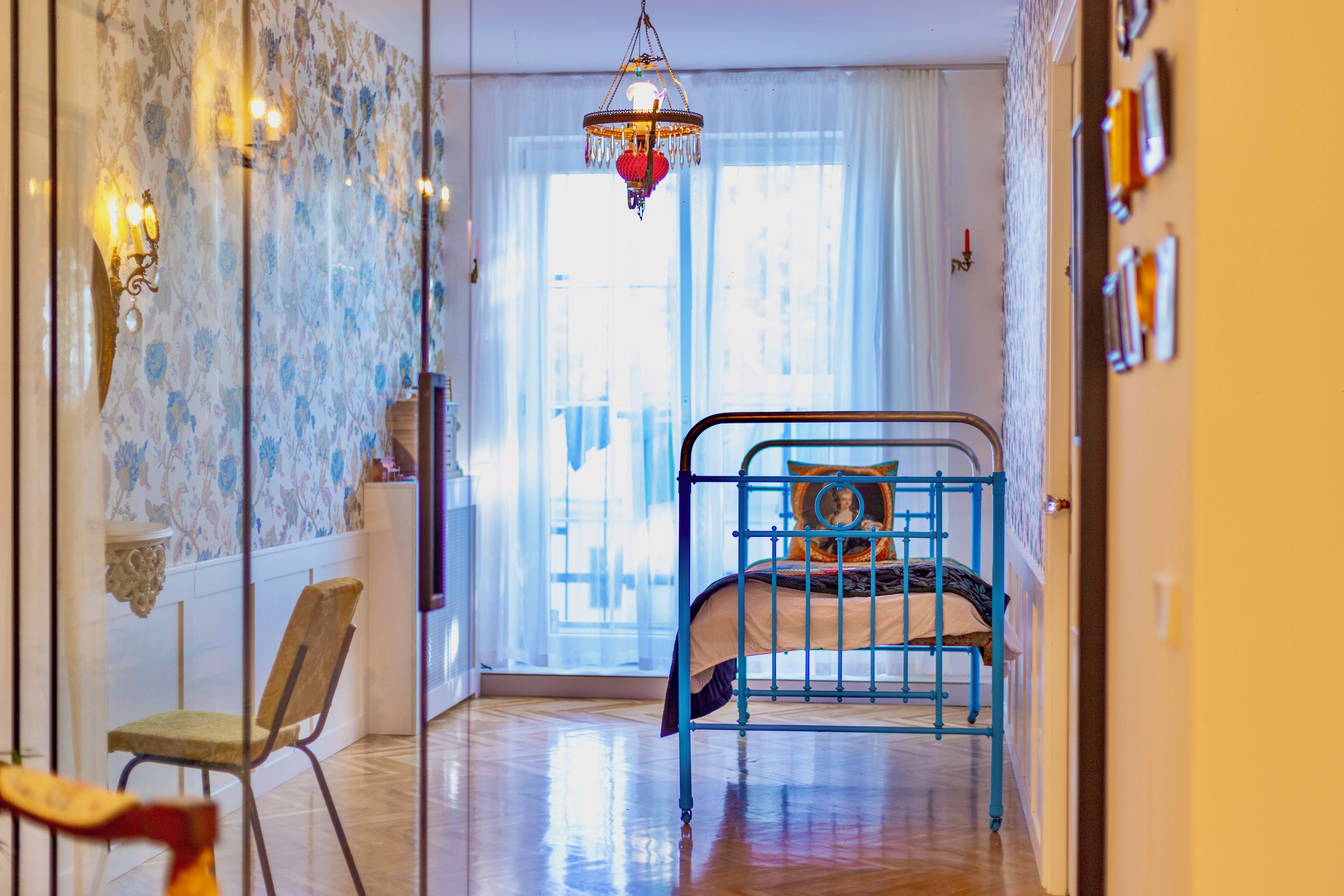 A bedroom with a bed, a chair, a hanging light fixture, and a window with curtains.