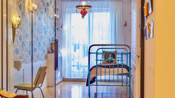 A bedroom with a bed, a chair, a hanging light fixture, and a window with curtains.