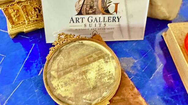 Une loupe est posée sur un livre, et en arrière-plan, on aperçoit le logo de « Art Gallery Suits ».