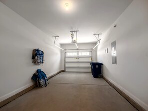 A clean, empty hallway with a garage door, a trash bin, and a ceiling-mounted light fixture.