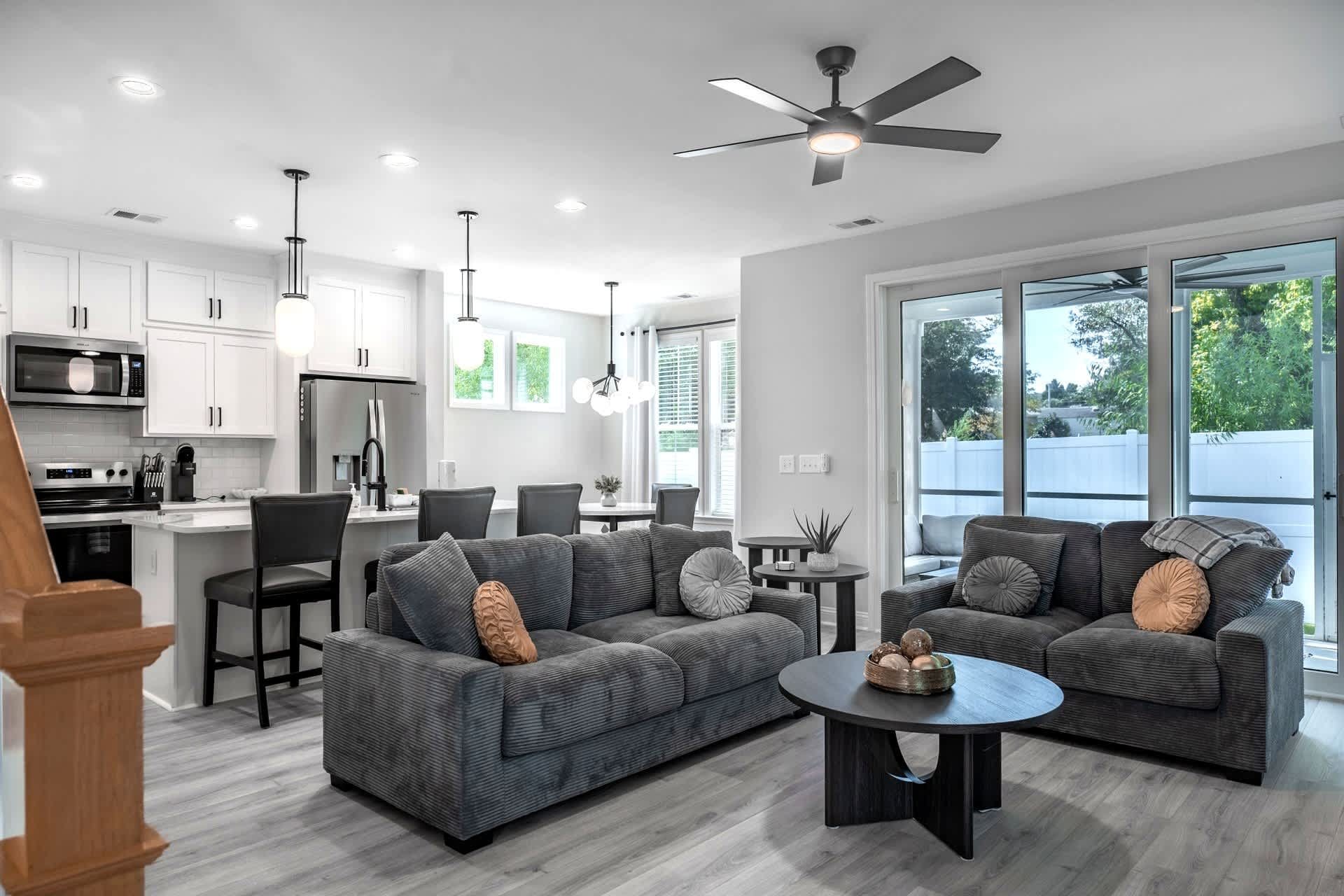 A modern kitchen with white cabinets, a microwave, and a dining area with a gray sofa and a small round table.