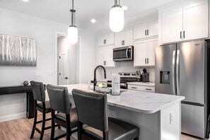 A modern kitchen with white cabinetry, stainless steel appliances, and a marble island with bar stools.