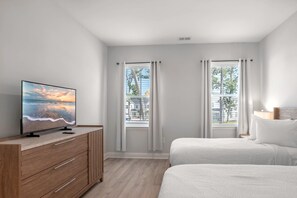 A bedroom with a TV on a wooden dresser, two beds, and a window with curtains.