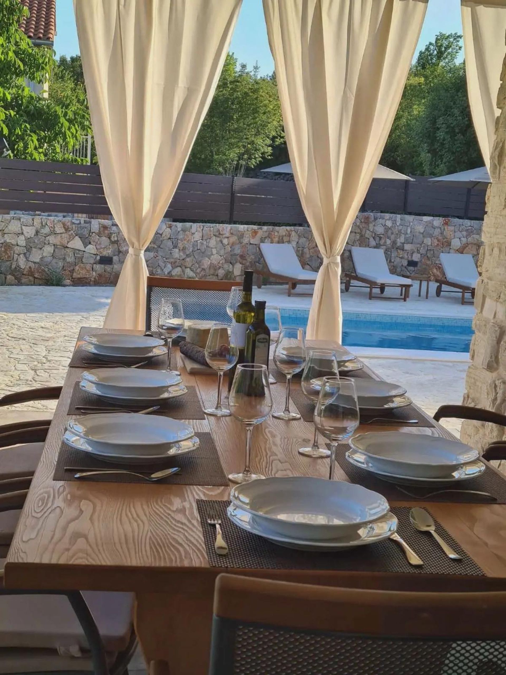 Un espace de restauration en plein air avec une table dressée pour un repas, donnant sur une piscine.