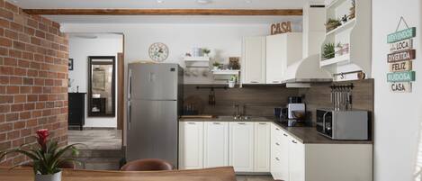 Een moderne keuken met witte kastjes, een roestvrijstalen koelkast en een houten eettafel met stoelen.