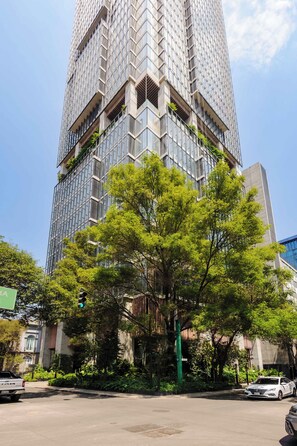 Un edificio alto con fachada de vidrio moderna, rodeado de árboles y vegetación.