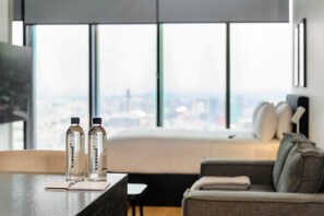 A modern hotel room with a large window, a bed, a sofa, and two water bottles on a table. - w* | Enchanting Loft in Juarez w/ Pool (Ciudad de México)