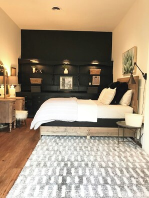A bedroom with a large bed, a dresser, a nightstand, and a wall-mounted shelf with decorative items. - The Brick Cottage - Boat Parking, Close to ATU (Russellville)