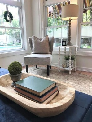 A room with a chair, a small table with books, a lamp, and a view of greenery outside. - The Brick Cottage - Boat Parking, Close to ATU (Russellville)