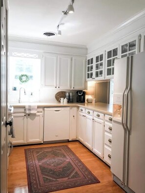 A kitchen with white cabinets, a refrigerator, a coffee maker, and a rug on the floor. - The Brick Cottage - Boat Parking, Close to ATU (Russellville)