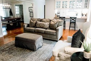 A living room with a sofa, ottoman, and a dining area with a table and chairs. - The Brick Cottage - Boat Parking, Close to ATU (Russellville)