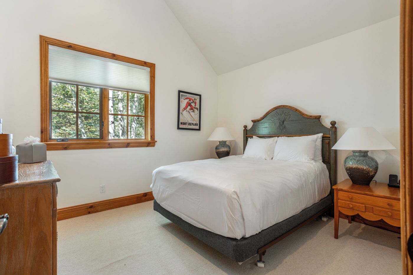 A bedroom with a bed, two bedside tables, a window, a framed picture, and a wooden dresser.