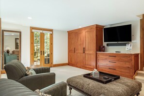 Uma sala de estar com sofá, apoio para os pés, armários de madeira, televisão e máquina de café.