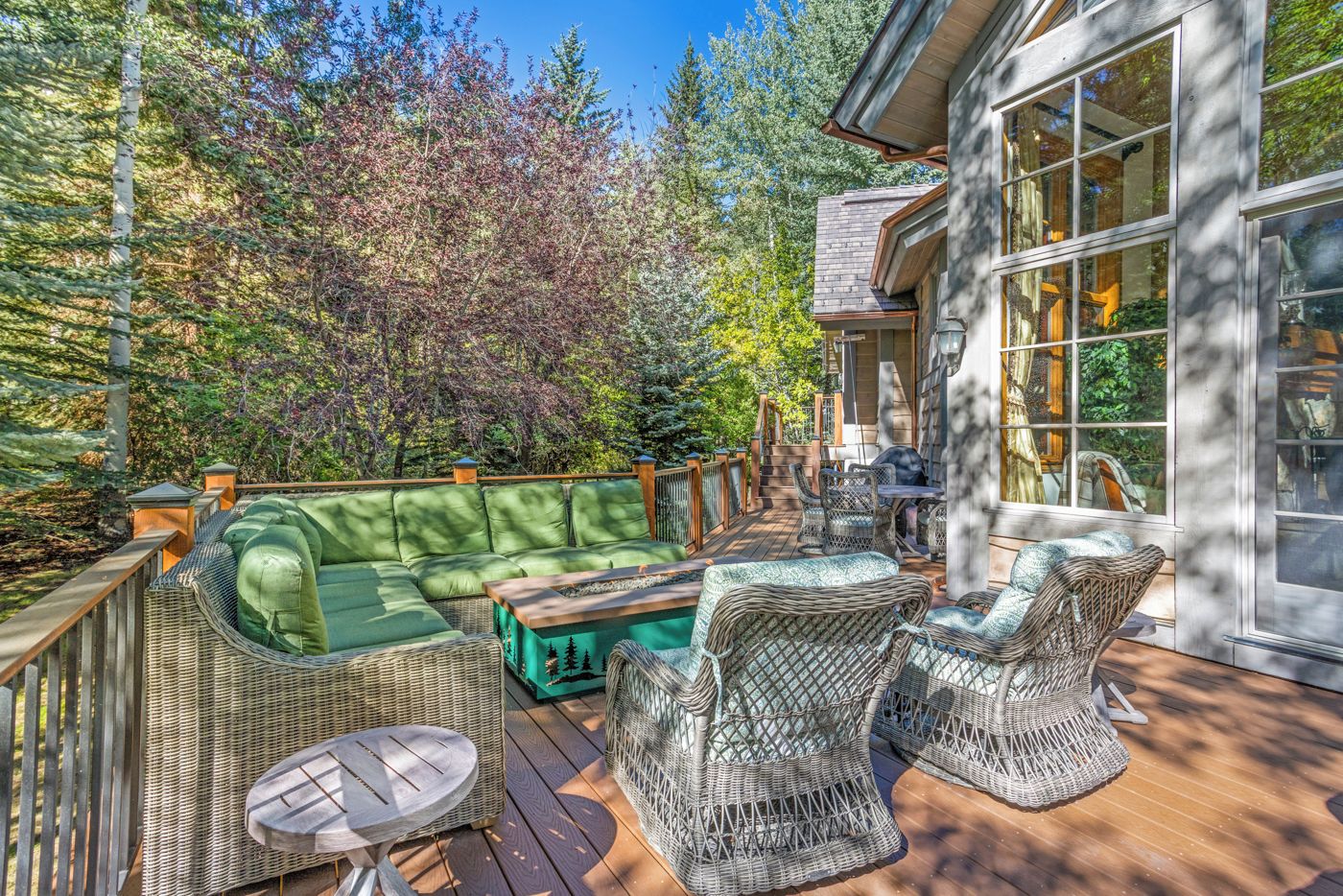 A covered outdoor deck with wicker furniture, a green sofa, and a dining table.