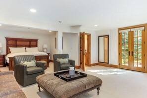 A spacious bedroom with a large bed, two armchairs, a small ottoman, and a wooden door leading to a balcony. - Newly Listed! 8BR Beaver Creek Home | Hot Tub (Avon)