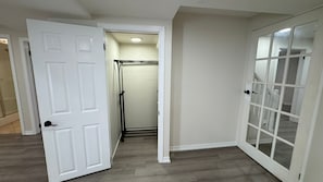 A hallway with a white door, a glass door, and a walk-in closet with a clothes rack. - Cozy,Large 2 Bedroom 1 Bathroom Separate Entrance Basement Apartment in Ancaster (Hamilton)