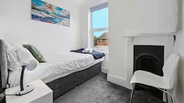 Een slaapkamer met een bed, een stoel, een nachtkastje, een schilderij aan de muur en een raam.