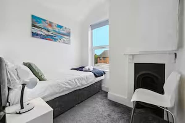 Quarto com cama, cadeira, mesa de cabeceira, quadro na parede e janela.