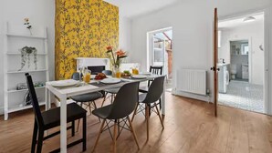 Een eetgedeelte met een tafel voor vier personen, een gele behangmuur en uitzicht op de keuken.