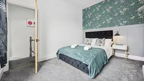 Een slaapkamer met een bed, nachtkastje en een bloemen behang.